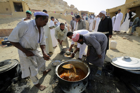 Cientos de hombres sentados en círculo en el desierto comiendo.
