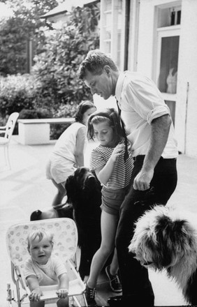 Attorney General Robert F. Kennedy (CR) playing with Caroline B. Kennedy (CL) and Christopher G. Kennedy (in stroller), while other family members are looking on.