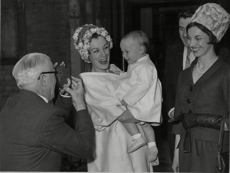 The Christening Of Anne Rogers Son At Hampstead Parish Church Tomothy Henry Is Held By His Mother Anne Rogers Watched By His Godmother Elizabeth Seal Gurgles Happily At Grandfather Henry Hall As He Makes A Film Record Of The Christening.