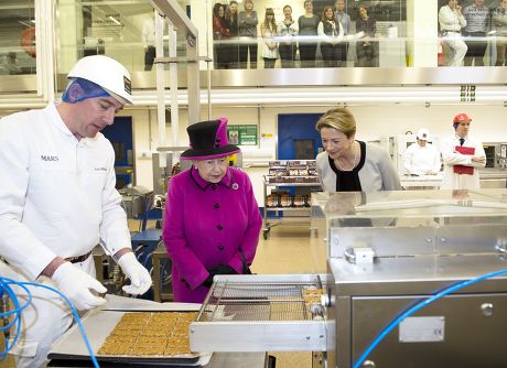 Queen Elizabeth II stands alongside President of Mars Chocolate UK Fiona Dawson (R) as Paul Milligan (L) puts Mars bars into a machine to cover them with chocolate in the pilot plant